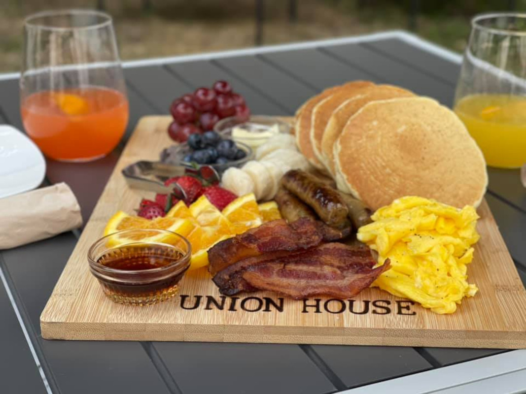 Food board with pancakes, ham, fruit and dip on the side.